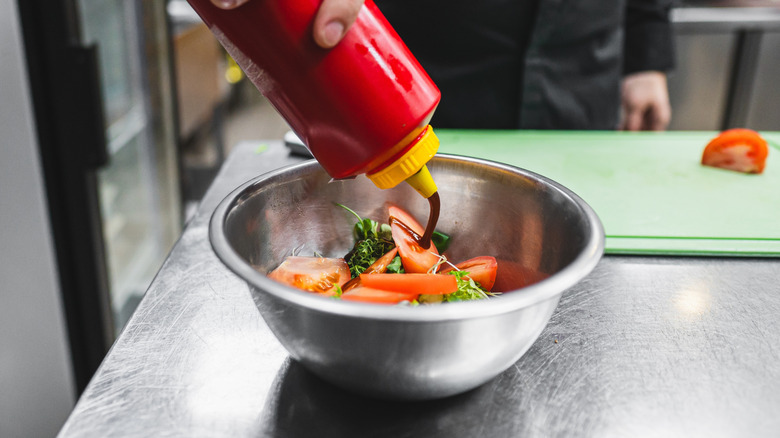 Person squeezing bottle of vinaigrette onto salad