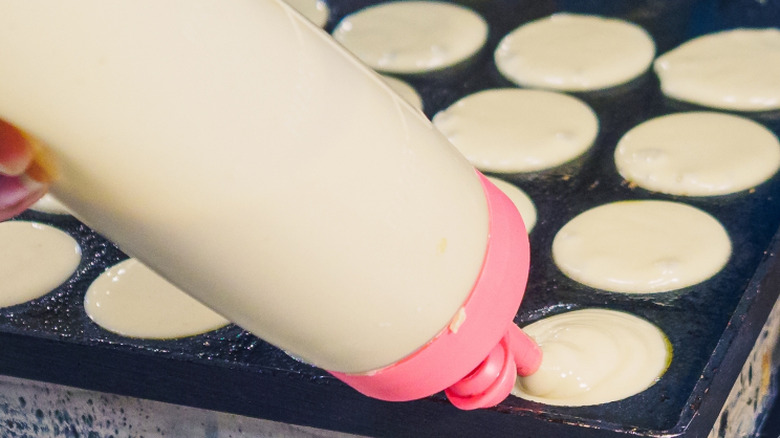 Person making miniature pancakes with squeeze bottle